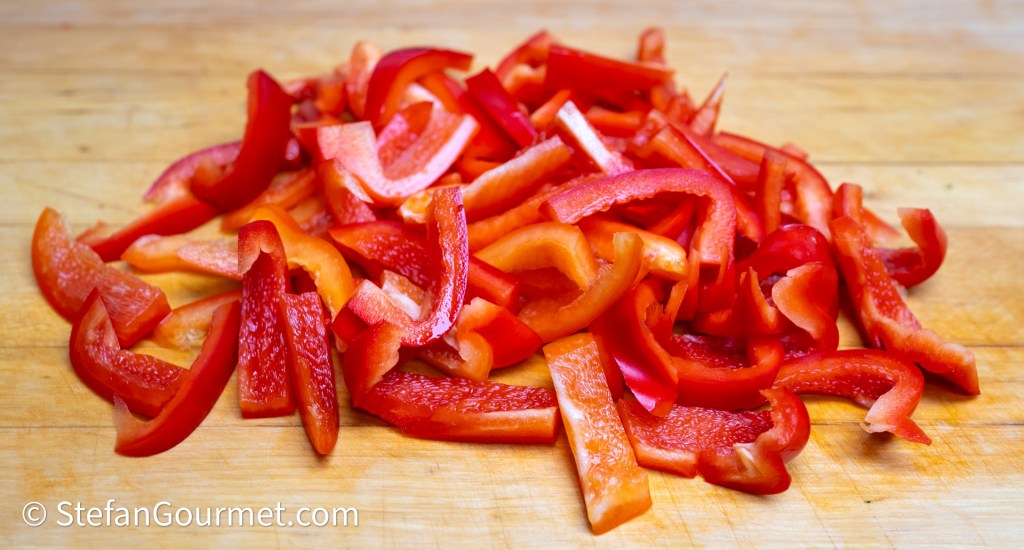 A pile of sliced red bell peppers on a wooden cutting board.