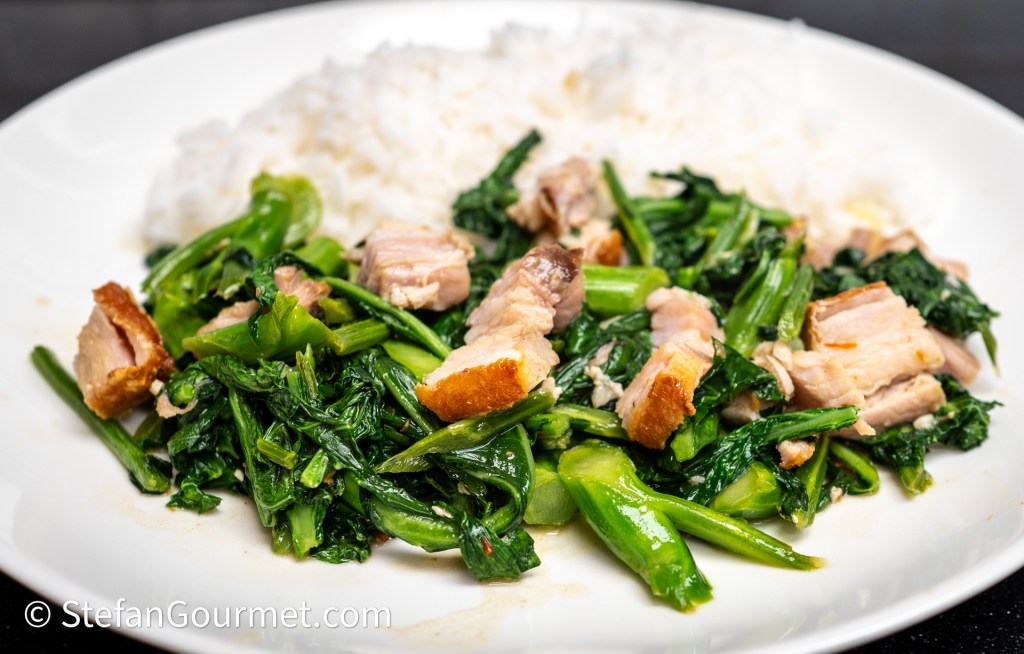 A plate of sautéed greens with pork and a side of white rice.