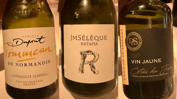 Three wine bottles on a table, featuring labels for Tommeau de Normandie, Jmsèleque Ratafia, and Vin Jaune from Côtes du Jura.