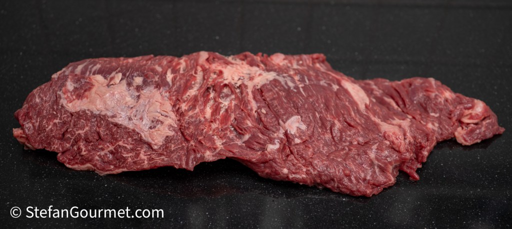 Raw flank steak resting on a dark countertop.