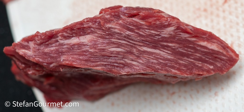 A close-up image of a piece of marbled raw beef, showcasing its texture and muscle fibers.