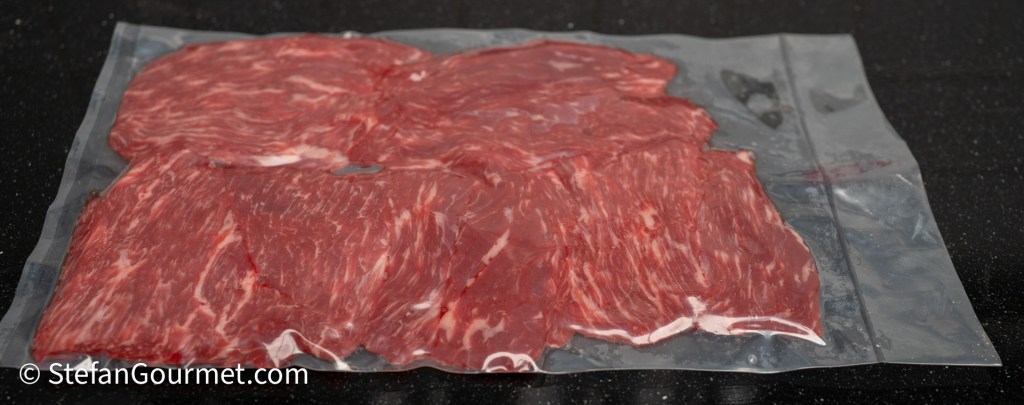 Vacuum-sealed package containing thinly sliced raw beef arranged neatly on a black countertop.