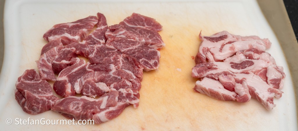 Sliced raw pork meat on a cutting board, with two distinct piles: one with larger pieces and another with smaller strips.