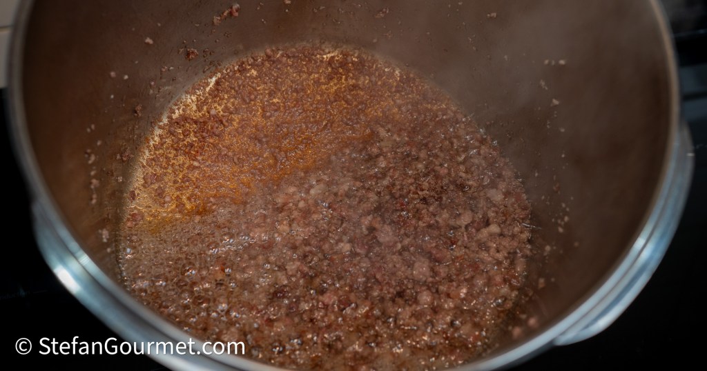 A close-up view of browned ground meat simmering in a pot, with steam rising and oil separating at the bottom.