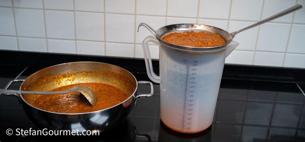 A saucepan containing a thick, reddish-brown sauce with a ladle, next to a measuring jug filled with the same sauce being strained.