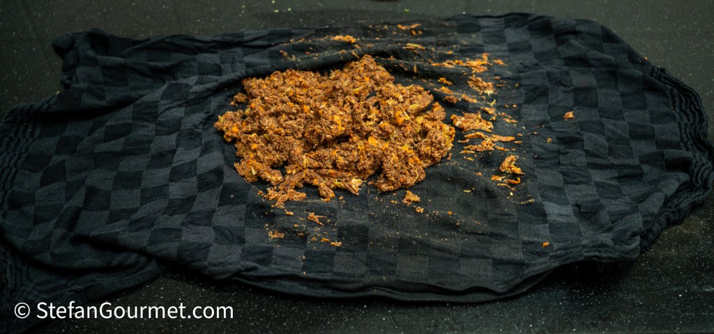 A black checkered kitchen towel with a mixture of reddish-brown food scattered on it.