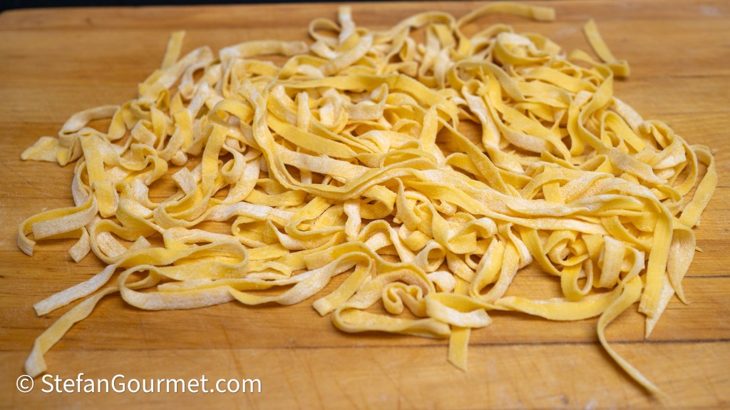 A pile of freshly made fettuccine pasta on a wooden surface.
