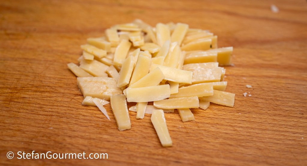 A pile of thinly sliced cheese on a wooden cutting board.