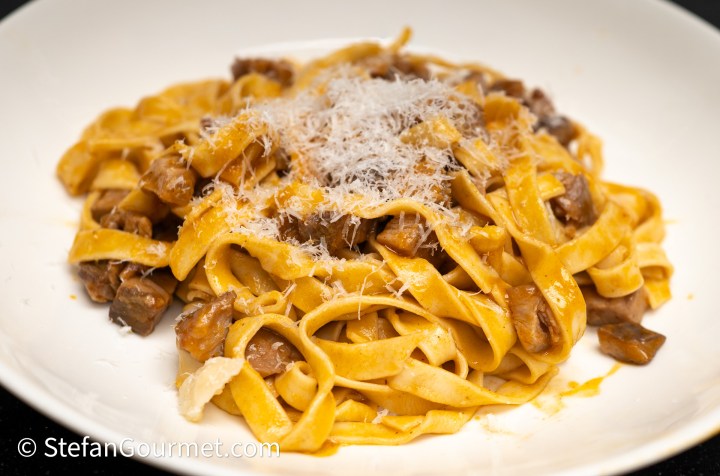 Plate of fettuccine pasta topped with grated cheese and a mushroom sauce.