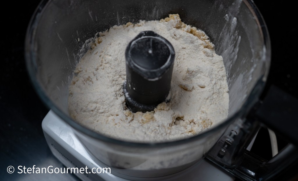 A close-up view of a food processor containing flour and a black bowl attachment.