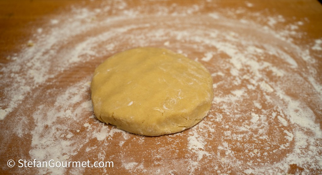 A round, uncooked dough disc on a wooden surface sprinkled with flour.