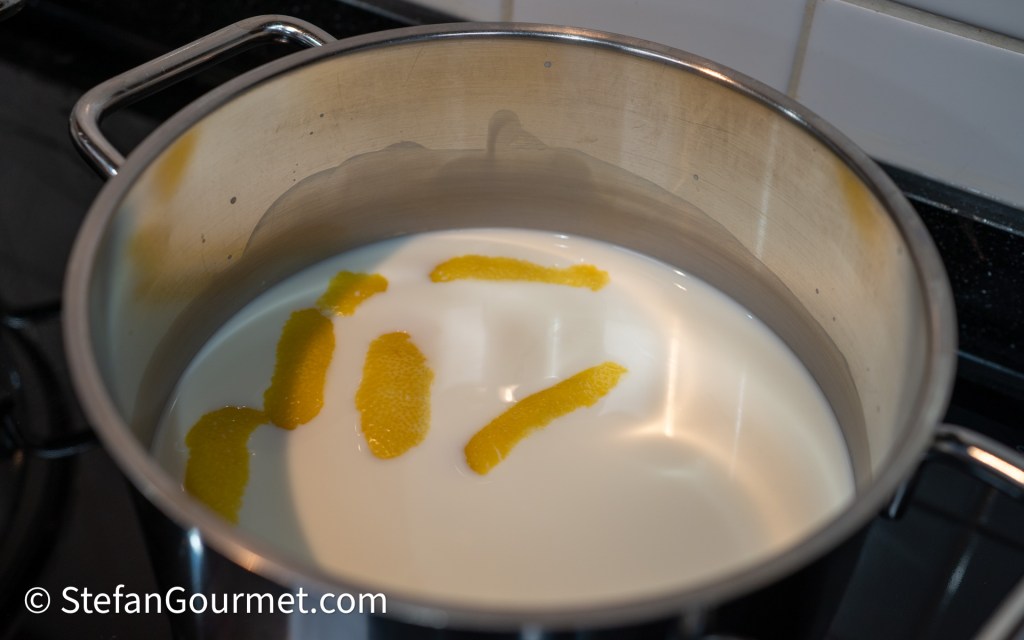 A stainless steel pot filled with milk and strips of orange peel, on a stovetop.