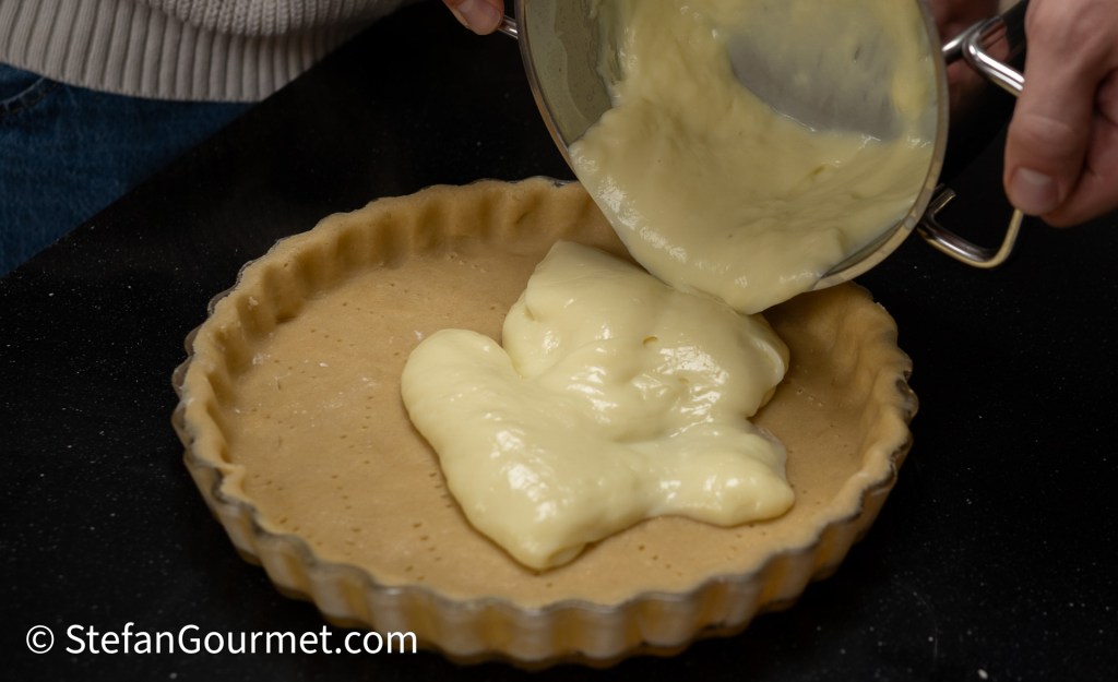 A person pouring creamy filling into an unbaked pie crust placed on a dark counter.