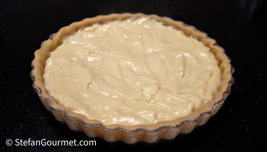 A freshly prepared cheesecake filling in a fluted tart shell, placed on a dark countertop.