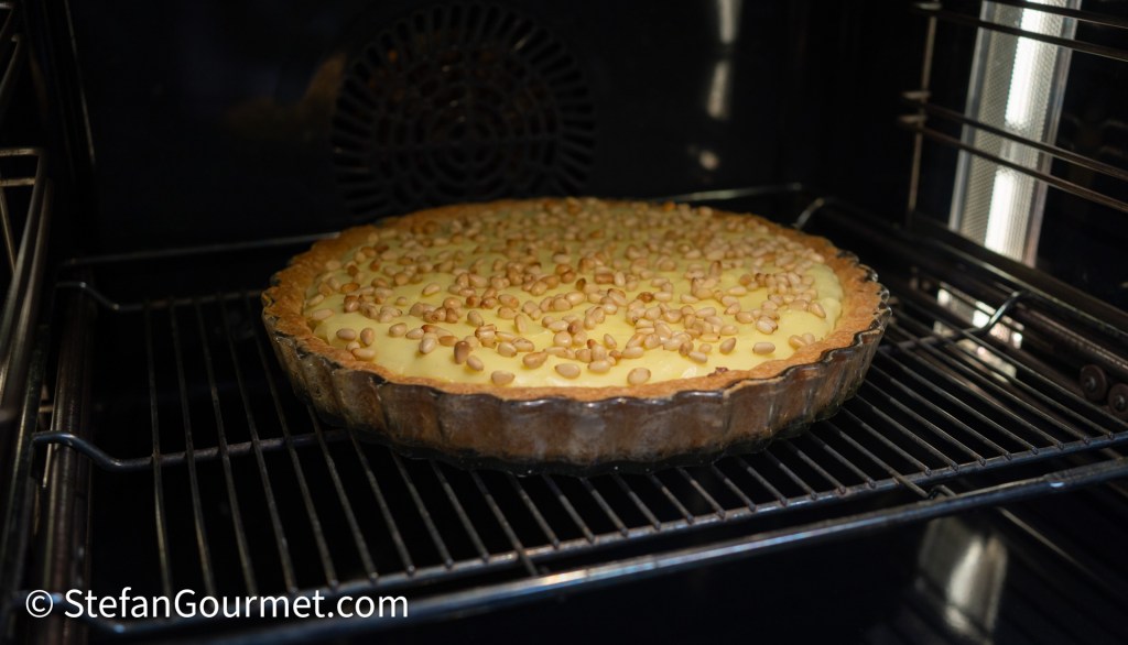 A freshly baked pie with a golden crust and a creamy filling topped with pine nuts, resting on the oven rack.