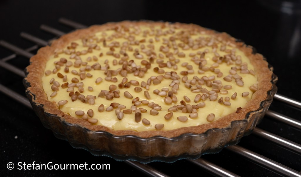 A freshly baked pie with a creamy yellow filling topped with toasted pine nuts, placed on a cooling rack.