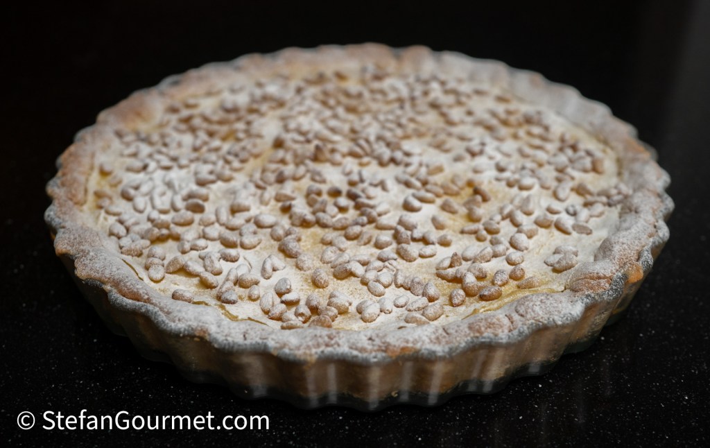A freshly baked pie with a dusting of powdered sugar, topped with small round pastry pieces, placed on a dark countertop.